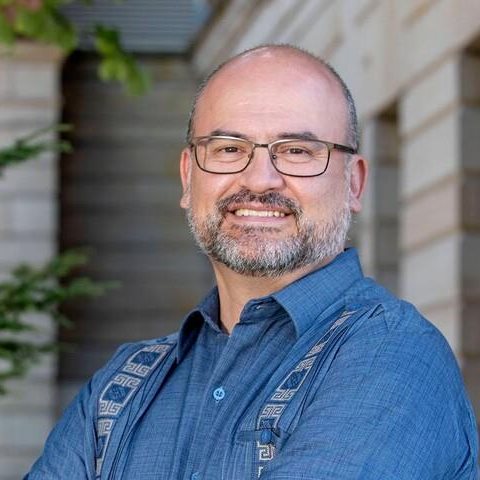 Middle aged man with glasses posses with arms crossed and smiles as the camera at a three quarters turn.