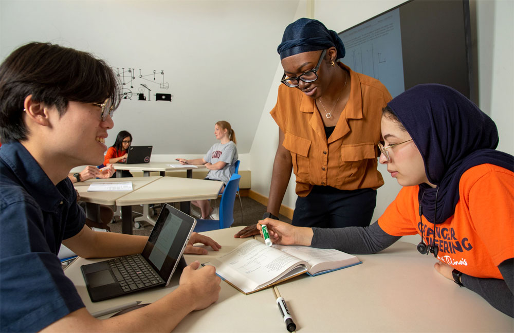 A peer tutor at the center for academic resources helps two students on their homework.